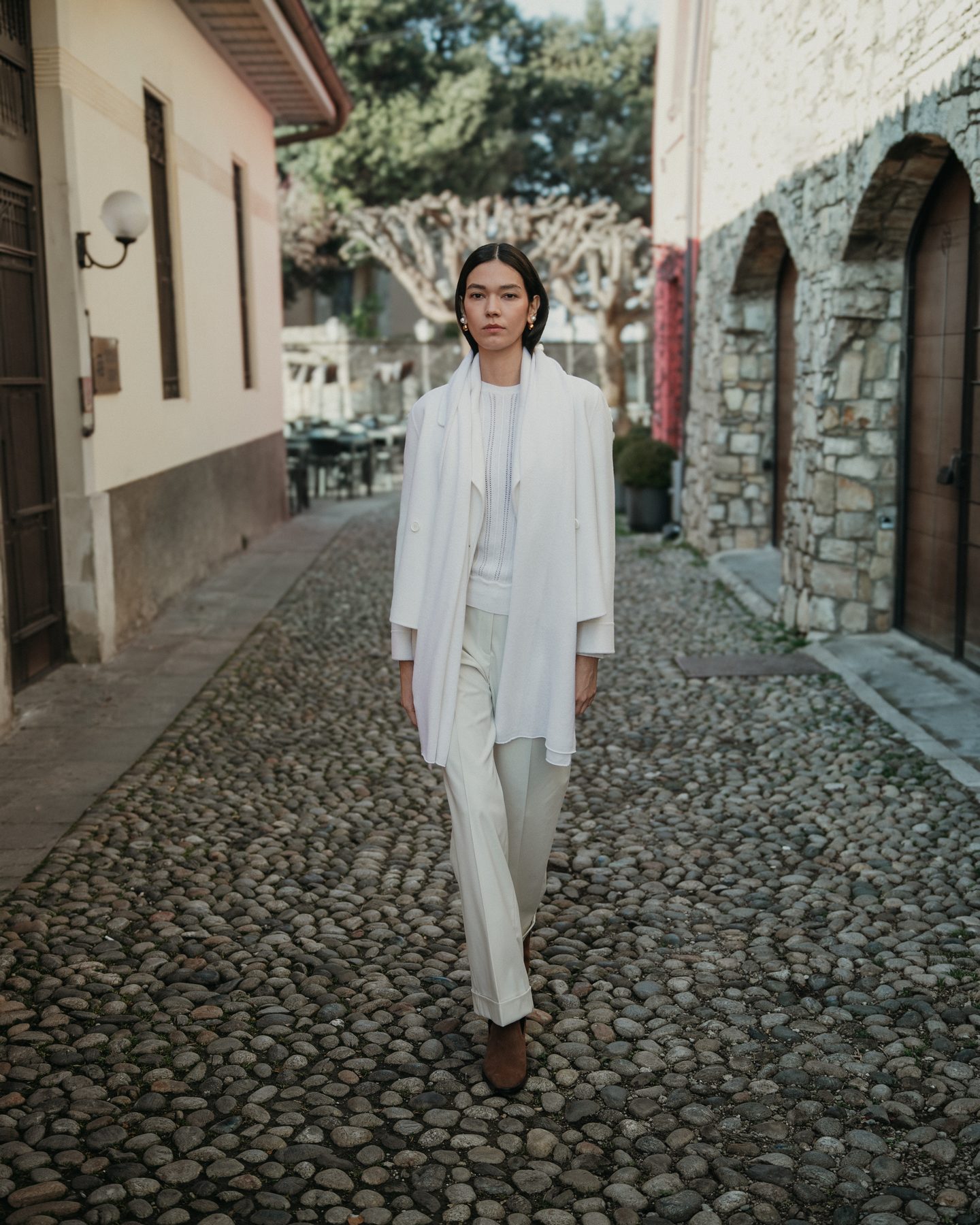 Look tutto avorio: cappotto, maglia e pantaloni in un vicolo acciottolato di Città Alta