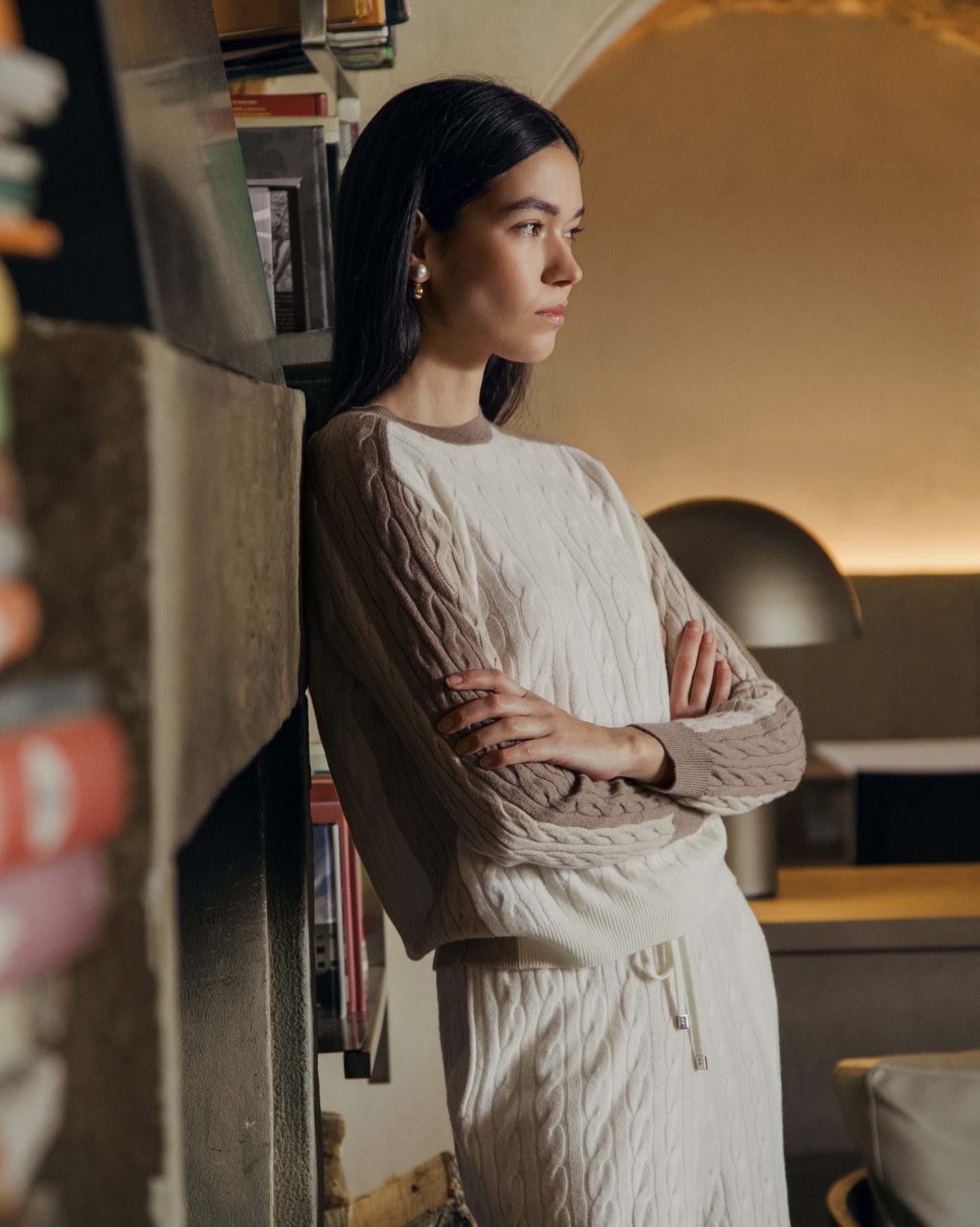 Pullover a trecce color panna in un interno con libreria