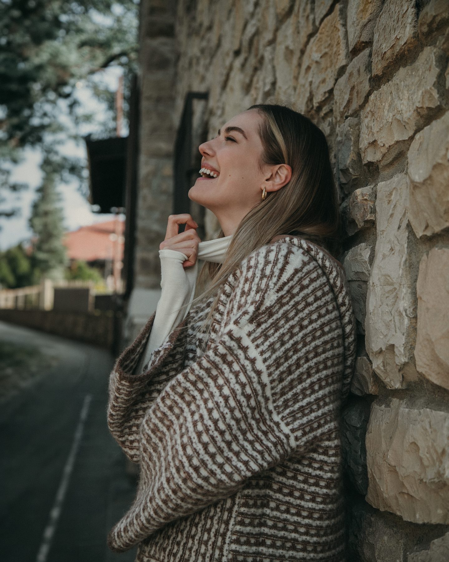 Cardigan in maglia jacquard bruno e avorio, appoggiata a un muro di pietra